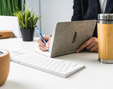 Person writing in a branded notebook beside a bamboo flask